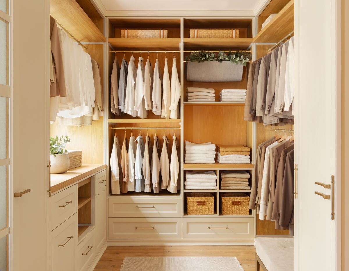 Walk-in closet with oak shelving, shirts hung by color, folded sweaters and woven storage baskets